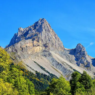 A mountain with trees in the foreground and blue sky